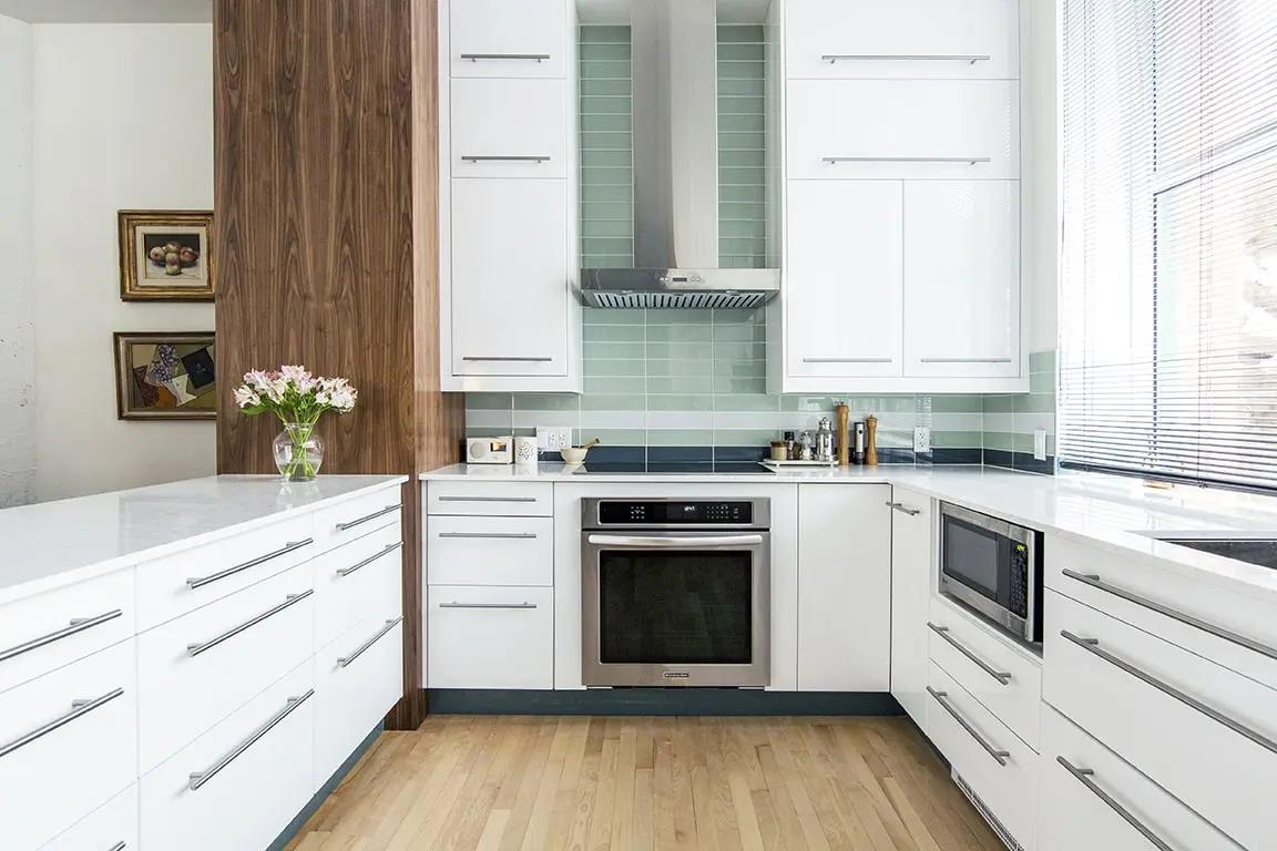 Bright, contemporary kitchen with central island, white quartz worktop and white cabinets. The black metal staircase adds an industrial touch to this space open to the living room. Perfect for lovers of lofts and open spaces.