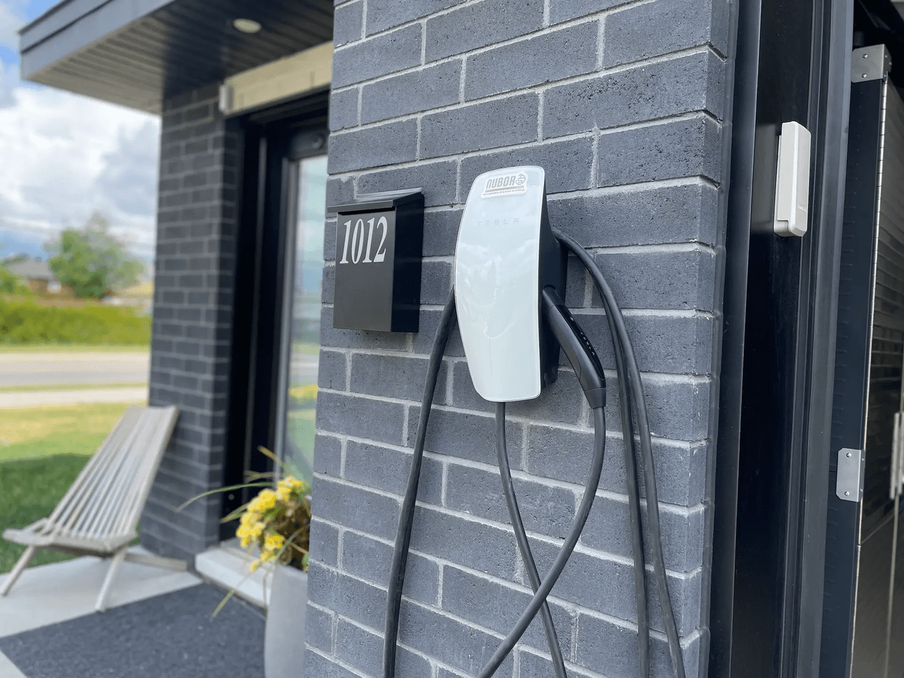 Wall-mounted electric vehicle charging station installed on modern gray brick exterior at house entrance