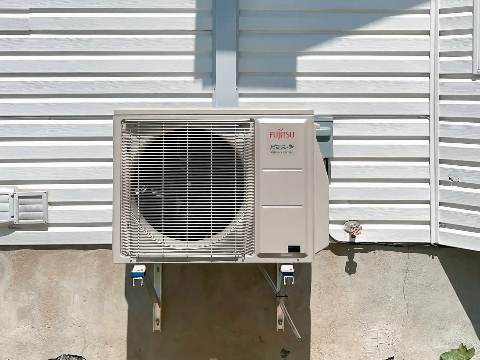 Fujitsu Halcyon outdoor heat pump unit installed on a white wall of a residential house, mounted on a metal bracket for a modern HVAC system, providing heating and cooling with optimal energy efficiency, ensuring thermal comfort.