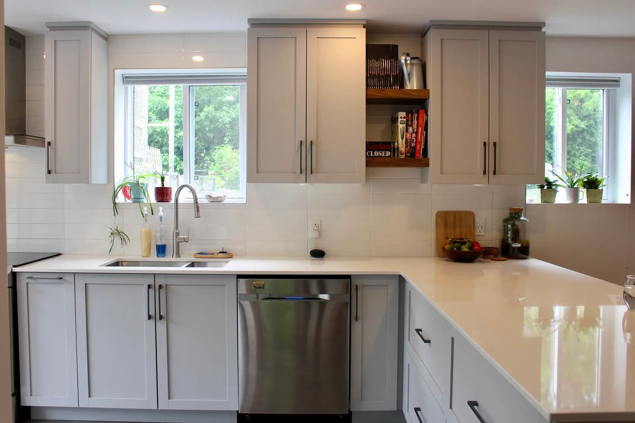 Bright contemporary kitchen with gray cabinets, white countertop, double sink, stainless steel dishwasher, windows and wood shelves.