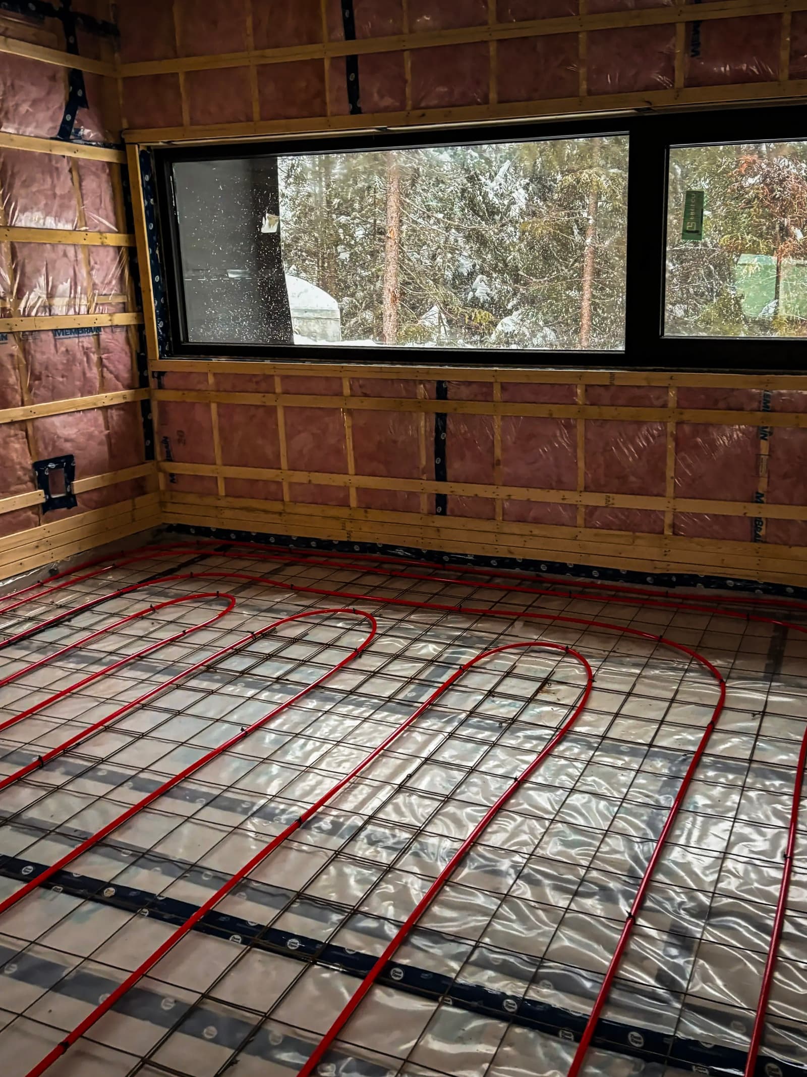 Underfloor heating system being installed in a room under construction with insulation and a panoramic window.