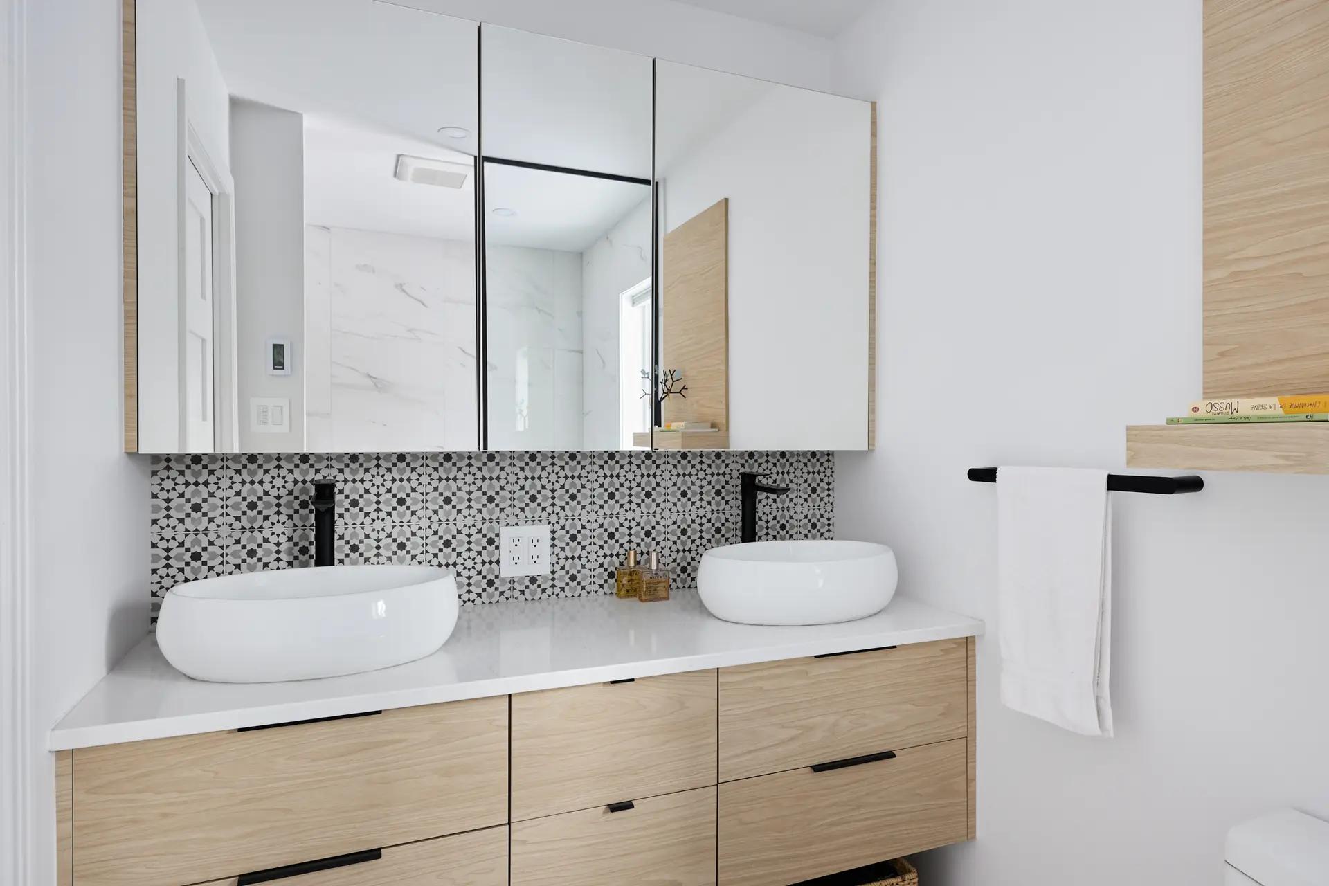 Bright bathroom with two ceramic vessel sinks on a wooden vanity, a custom mirror, and mosaic tile walls.