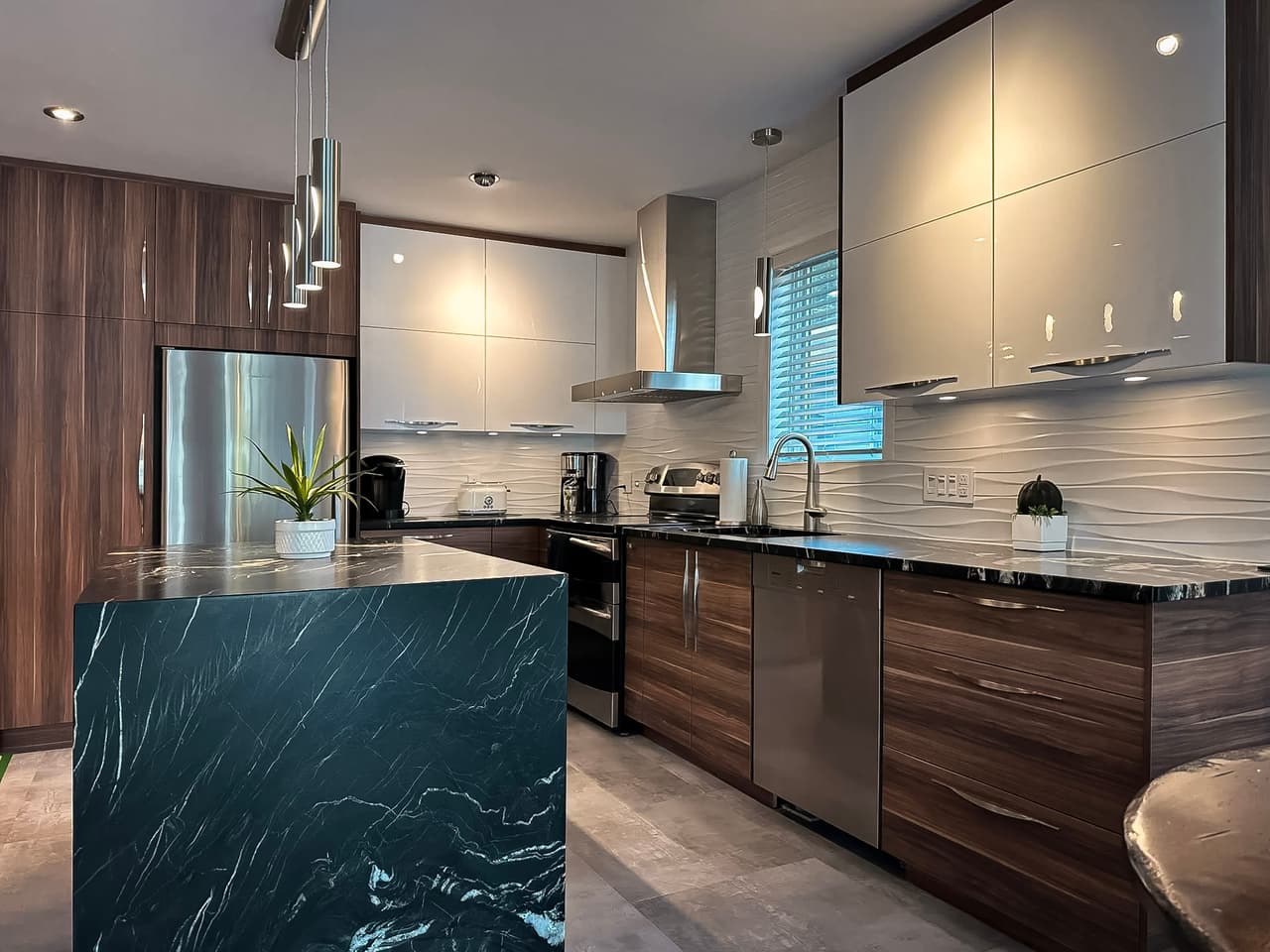 Modern kitchen with a black marble island, wood and glossy white cabinets, stainless steel appliances, and pendant lighting.