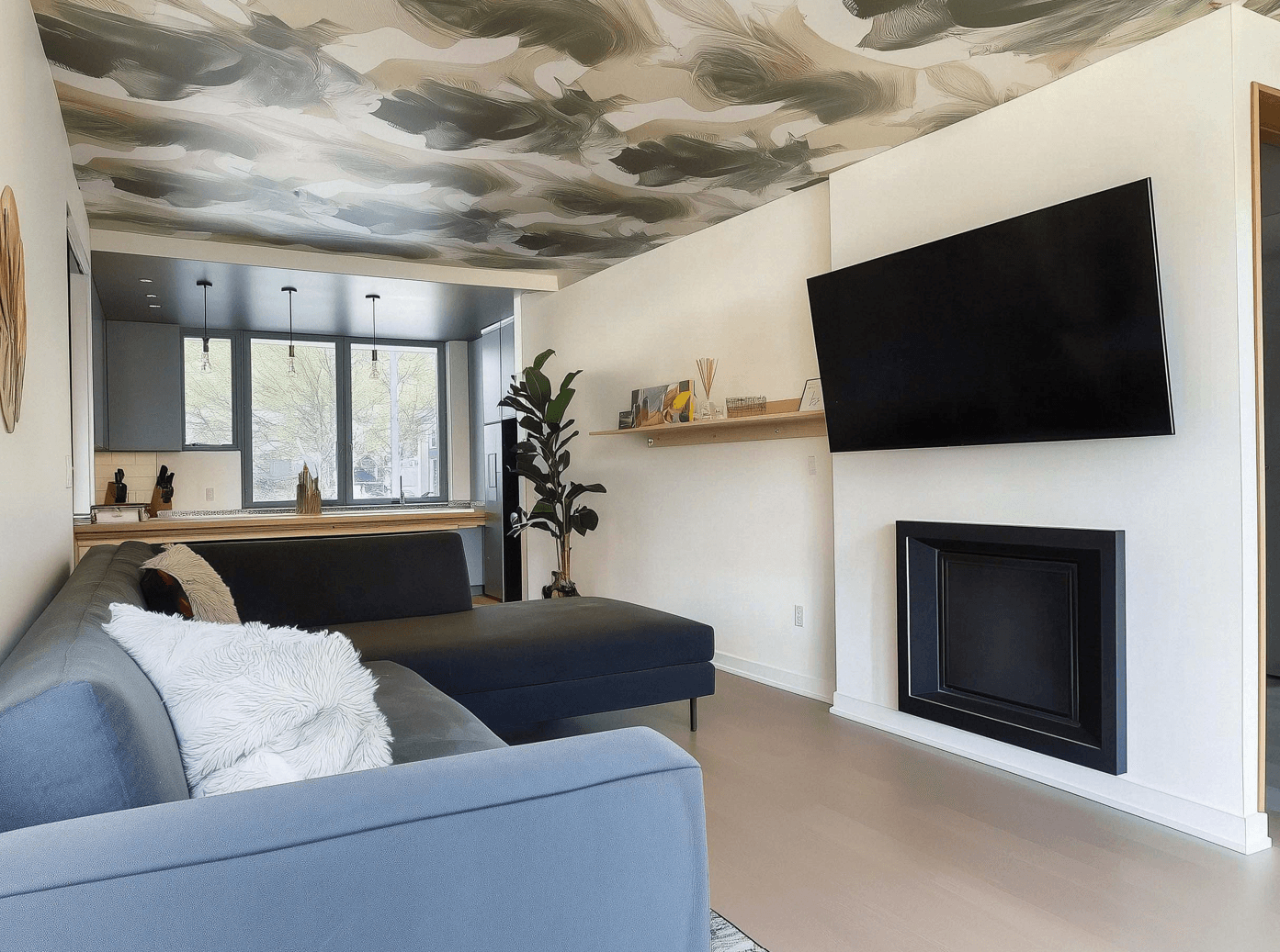Modern living room with sectional sofa, wall-mounted TV, black built-in fireplace, artistic ceiling and view of a bright kitchen with panoramic windows.