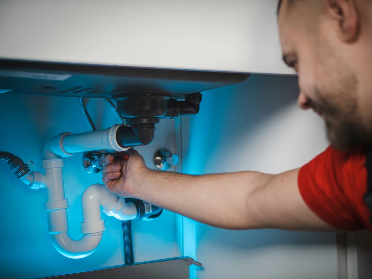Plumber repairing pipes under a sink with white trap and visible fittings