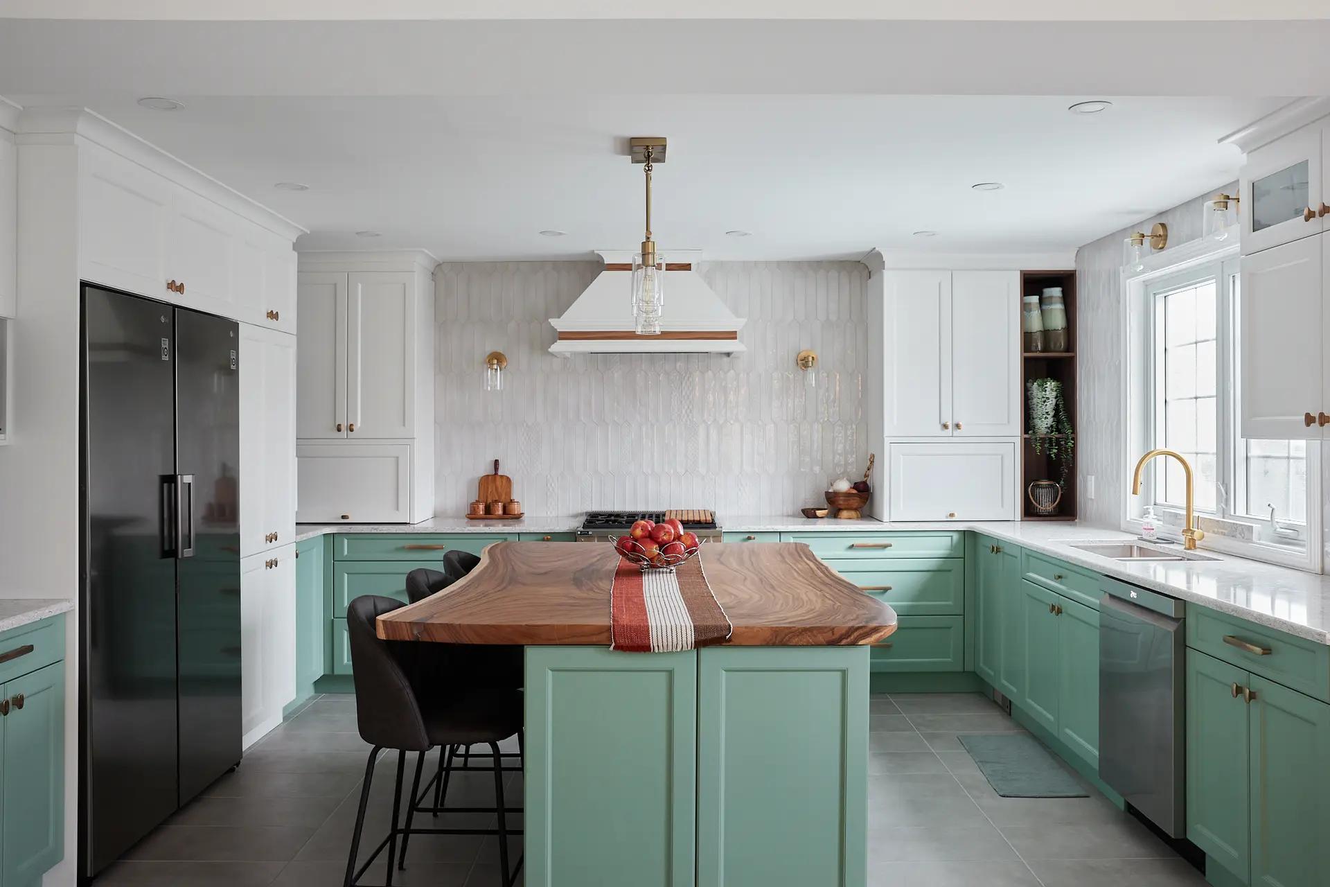 Transitional-looking Montréal kitchen, featuring a wood veneer central island with sleek lines. The mint green cabinetry and copper pulls make for a cool, elegant setting. The textured backsplash and neutral ceramic floor tiles create an interesting contrast.