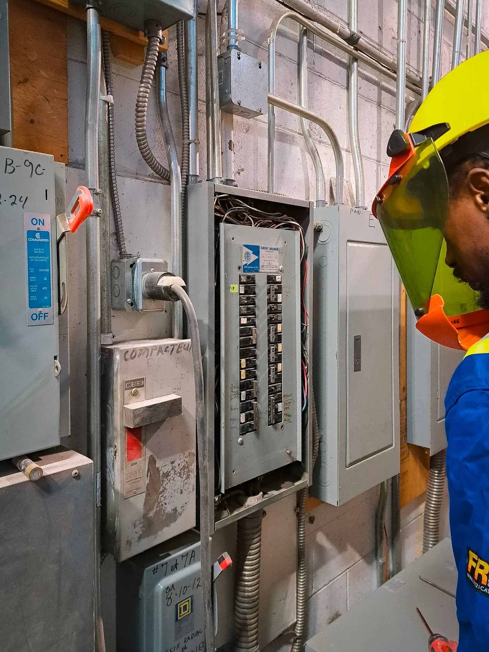 Electric technician with protective gear inspecting an industrial electrical panel