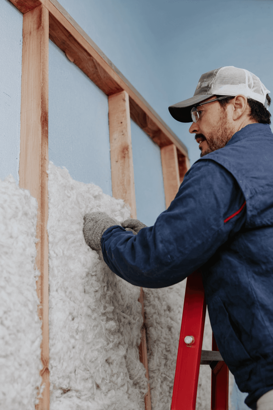 Worker installing fiber insulation inside a wood framed interior wall to improve thermal and acoustic insulation in a home