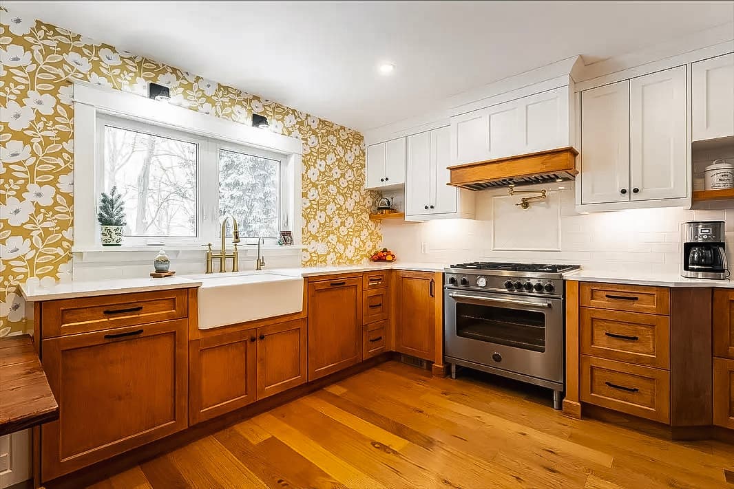 Rustic kitchen with wooden cabinets, yellow floral wallpaper, white farmhouse sink, white quartz countertops, and stainless steel stove.