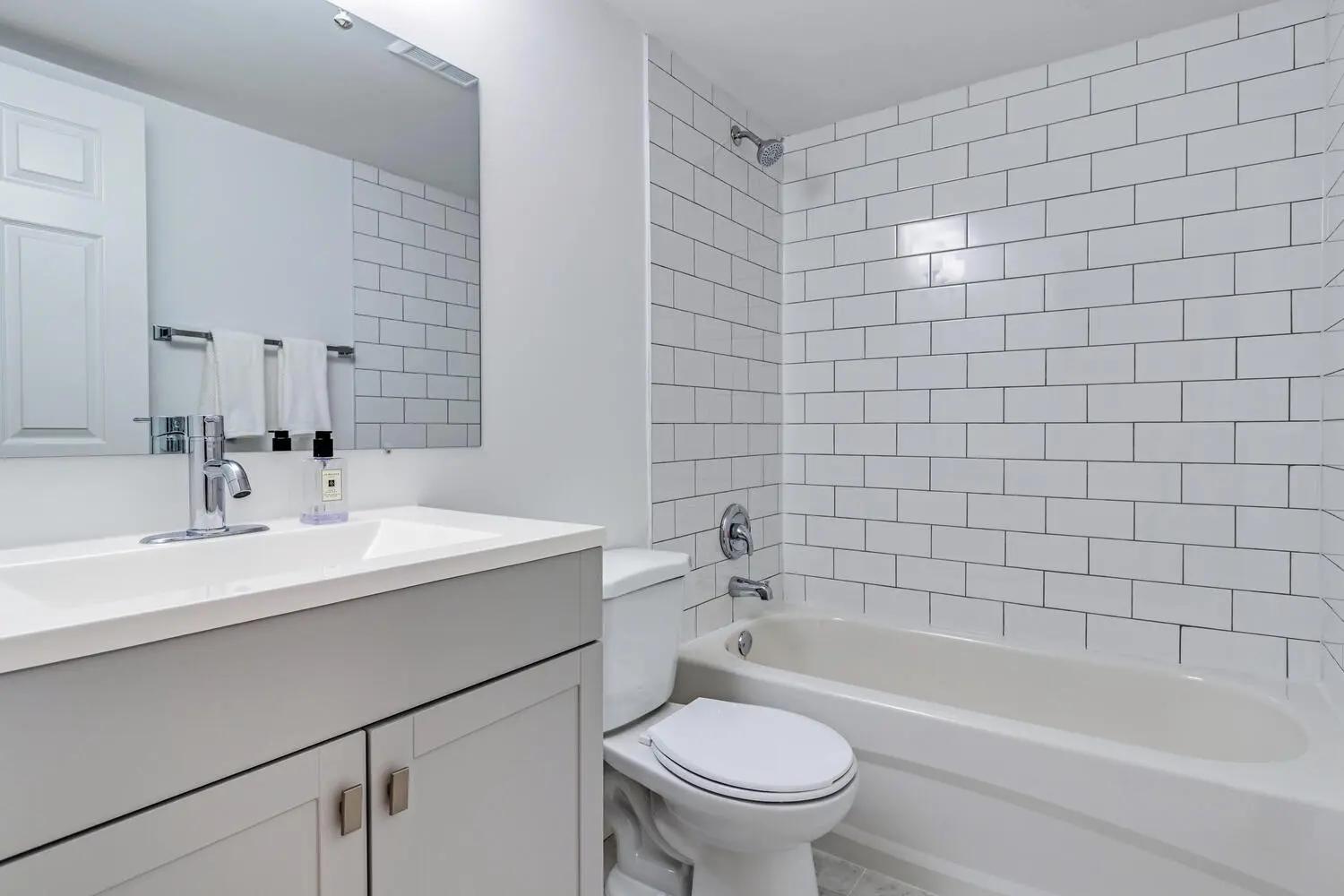 Clean and functional bathroom with a bathtub and shower, white tiled walls, and storage cabinets.