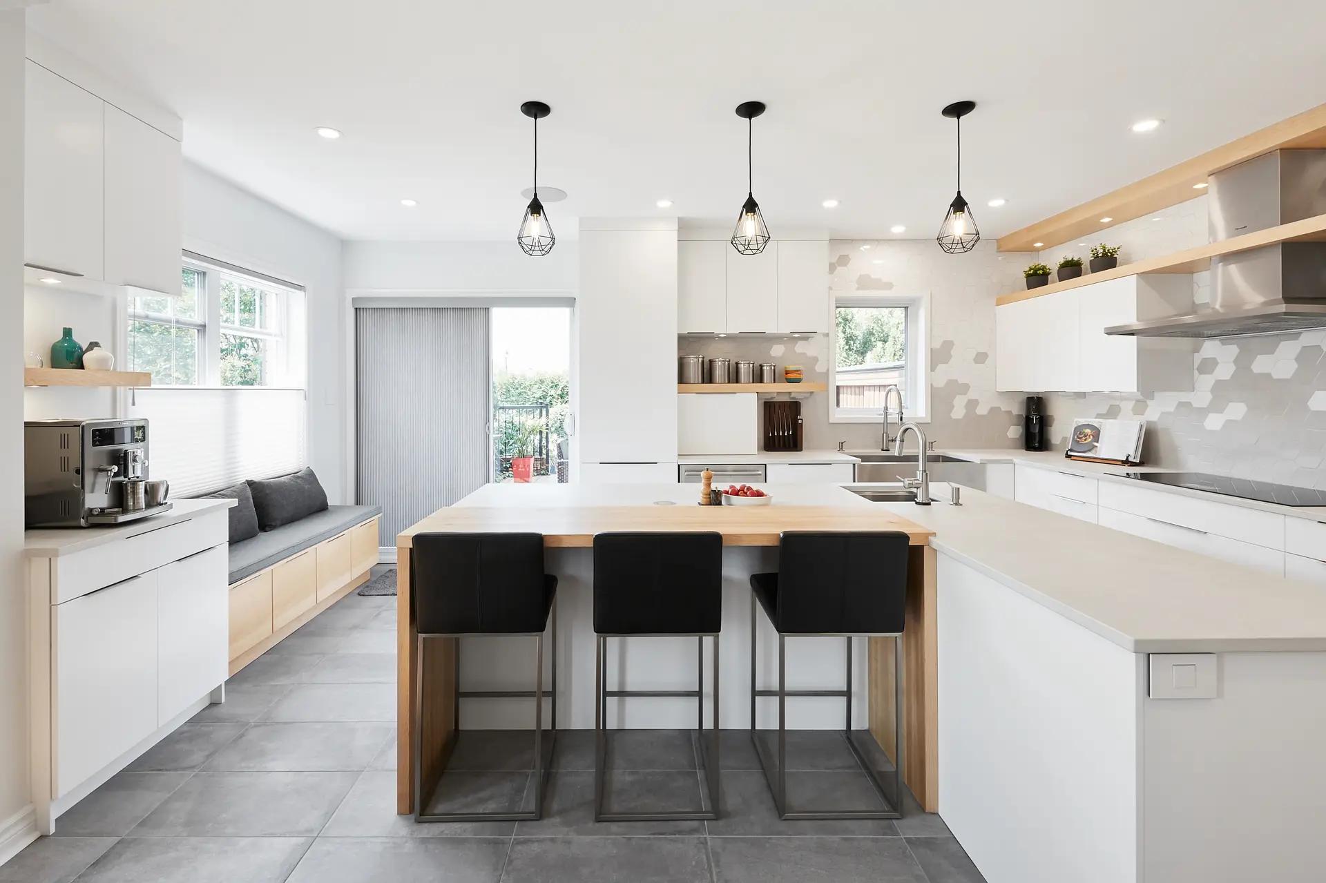 Scandinavian-style kitchen in Montreal, featuring a spacious center island with black barstools, minimalist white cabinets and a geometric mosaic backsplash. The gray ceramic floor adds a touch of warmth to the space.