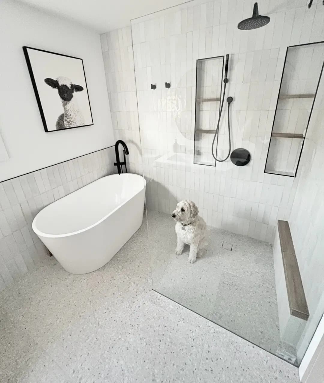 Modern minimalist bathroom featuring a white freestanding bathtub, glass walk-in shower, matte black fixtures, textured white wall tiles, recessed shower niches and terrazzo-style flooring, with a white dog in a bright contemporary interior