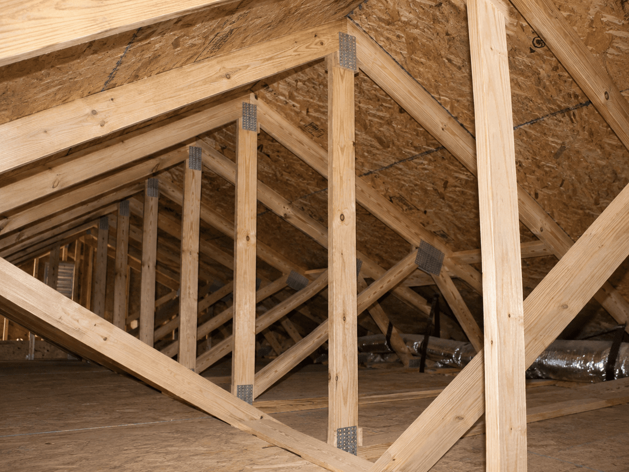Wood roof framing inside a residential attic with trusses, studs, bracing and structural wood sheathing