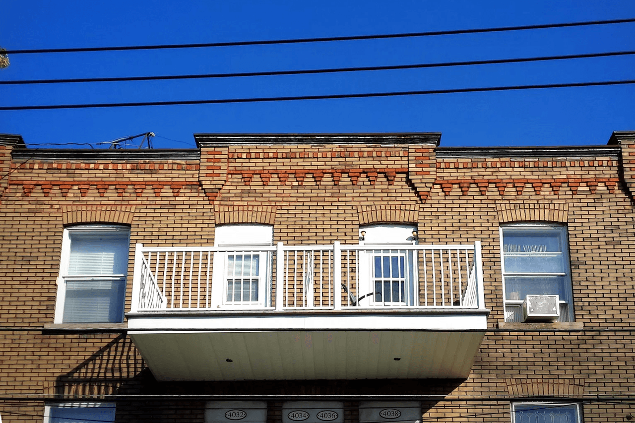 Brick facade of a residential building with white balcony and symmetrical windows under clear blue sky