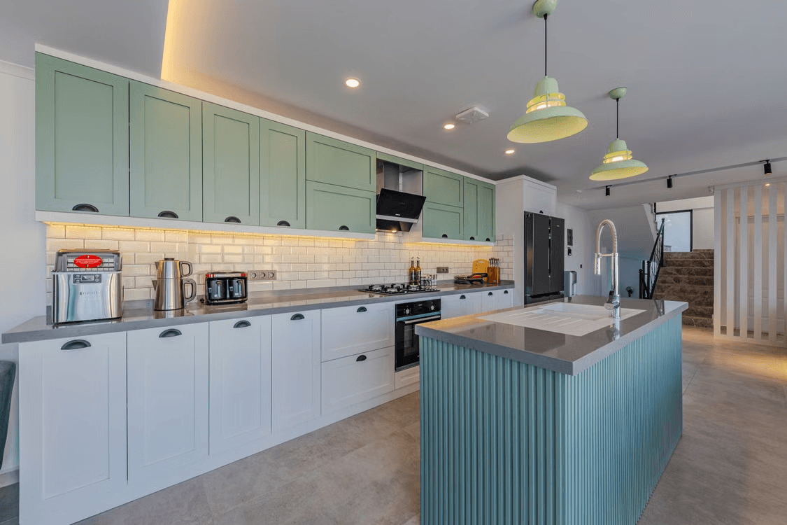 Contemporary kitchen with sage green and white cabinets, a large fluted central island, gray countertop, black appliances, pendant lighting, and subway tile backsplash.