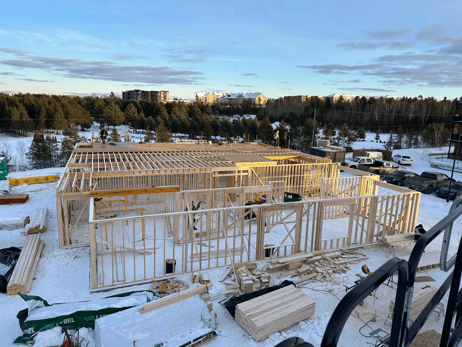View of a residential construction site with a wooden frame under assembly on a snowy landscape.