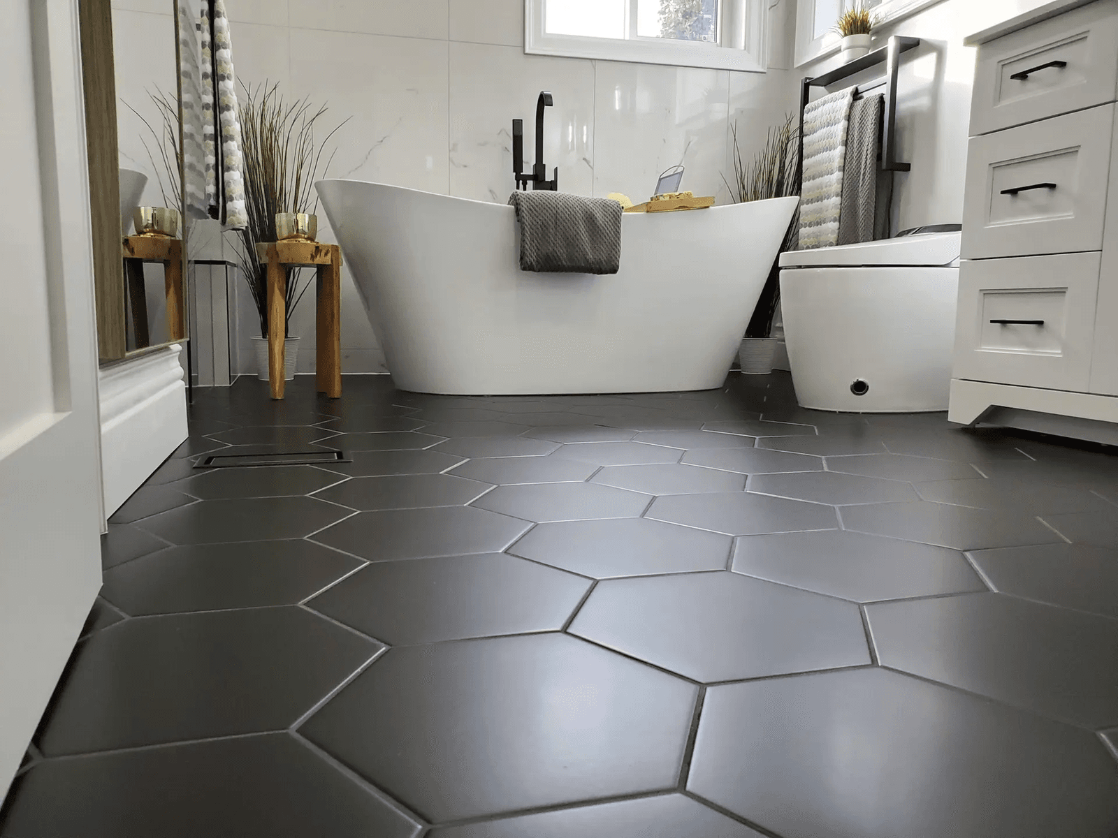 Contemporary bathroom with a white freestanding bathtub, matte black fixtures, dark grey hexagonal floor tiles, and marble-look walls.