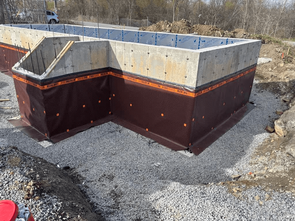 Residential concrete foundation with drainage and waterproofing membrane installed around the walls over a gravel base before backfilling