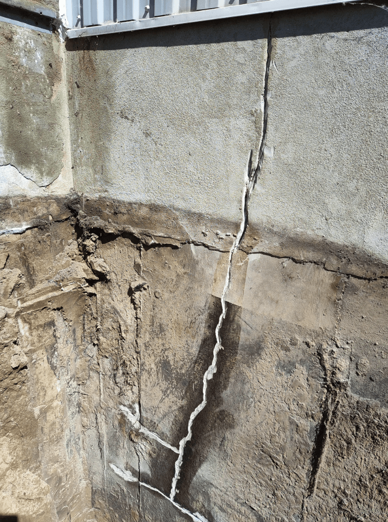 Significant vertical crack in an excavated concrete foundation showing signs of structural deterioration.