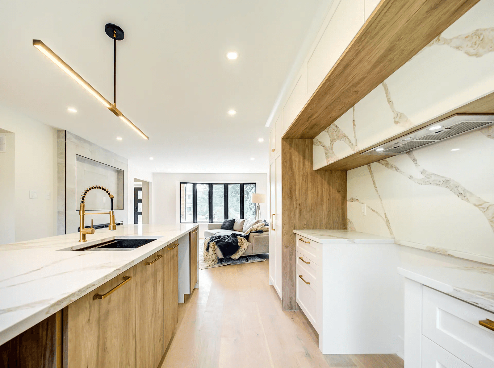 right modern kitchen with a large wood island, white marble-look countertop, gold faucet, integrated range hood and contemporary lighting