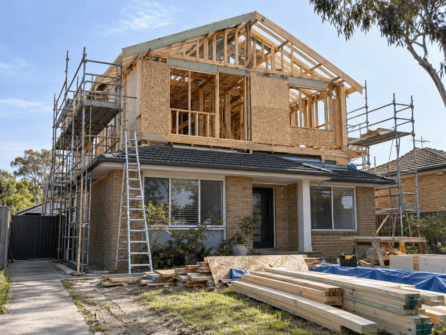 House second-storey addition under construction with exposed timber framing, structural panels, roof framing and scaffolding surrounding the building