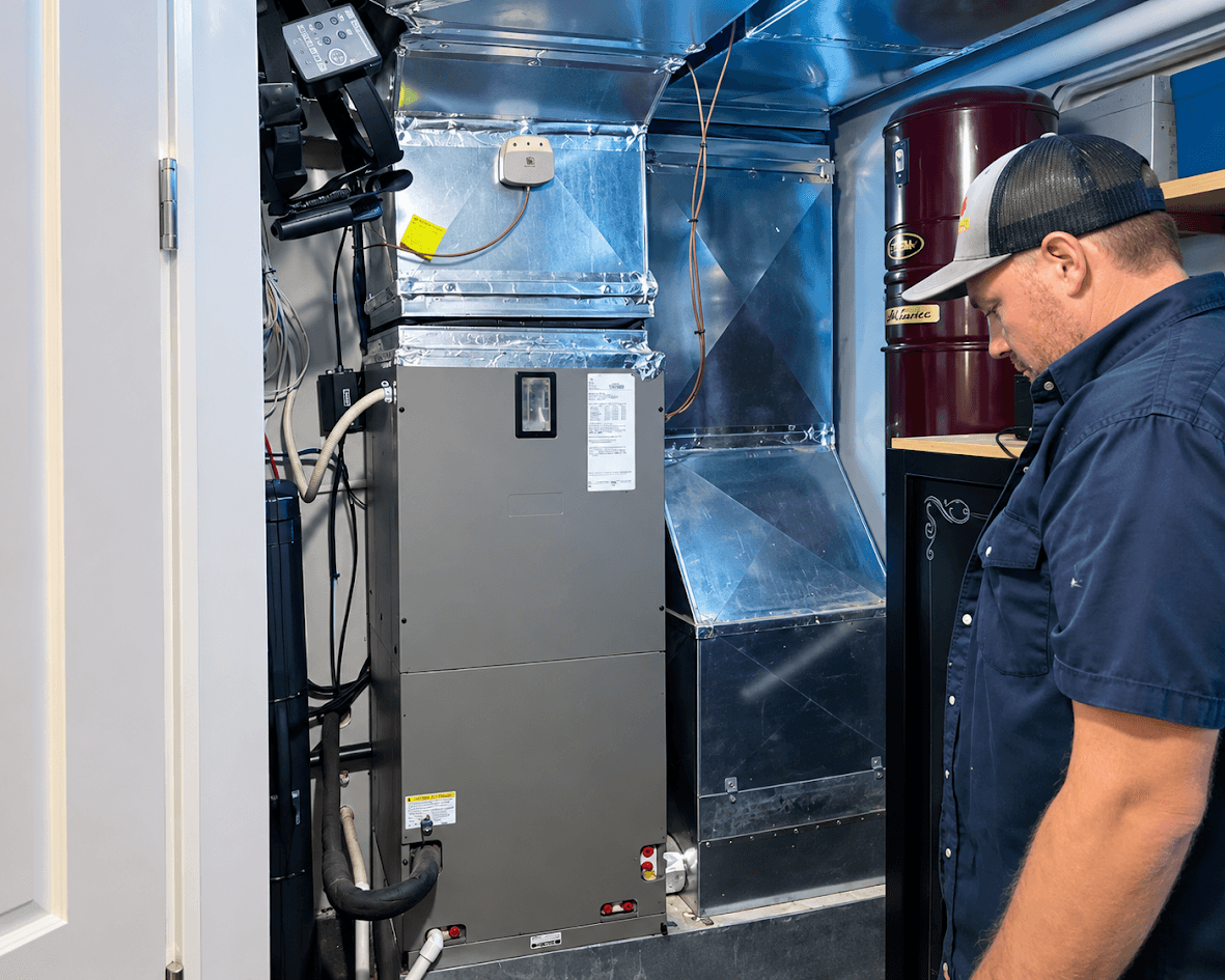 Heating and air conditioning technician inspecting a central system with mechanical unit, metal ventilation ducts, piping and technical equipment in a residential mechanical room.