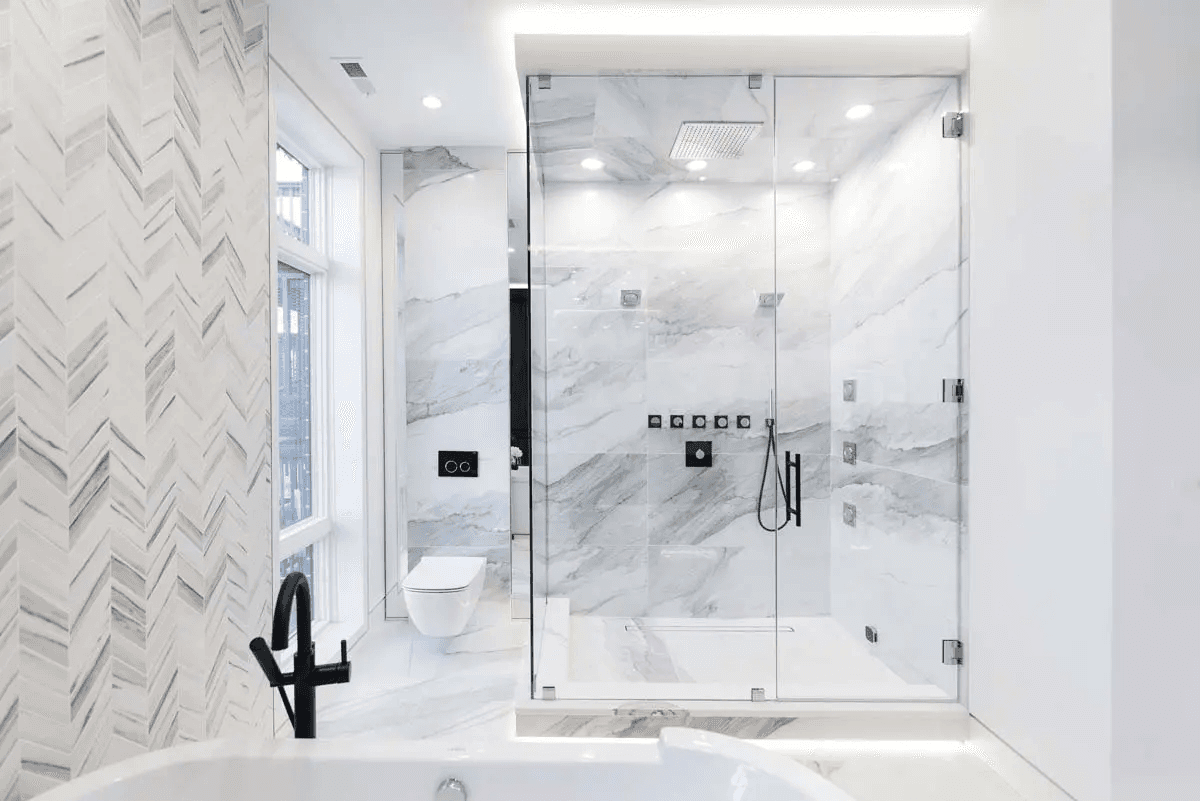 Modern luxury bathroom featuring a glass-enclosed shower, white marble walls, herringbone tile patterns, black fixtures, white bathtub, and recessed lighting for a clean, bright design.