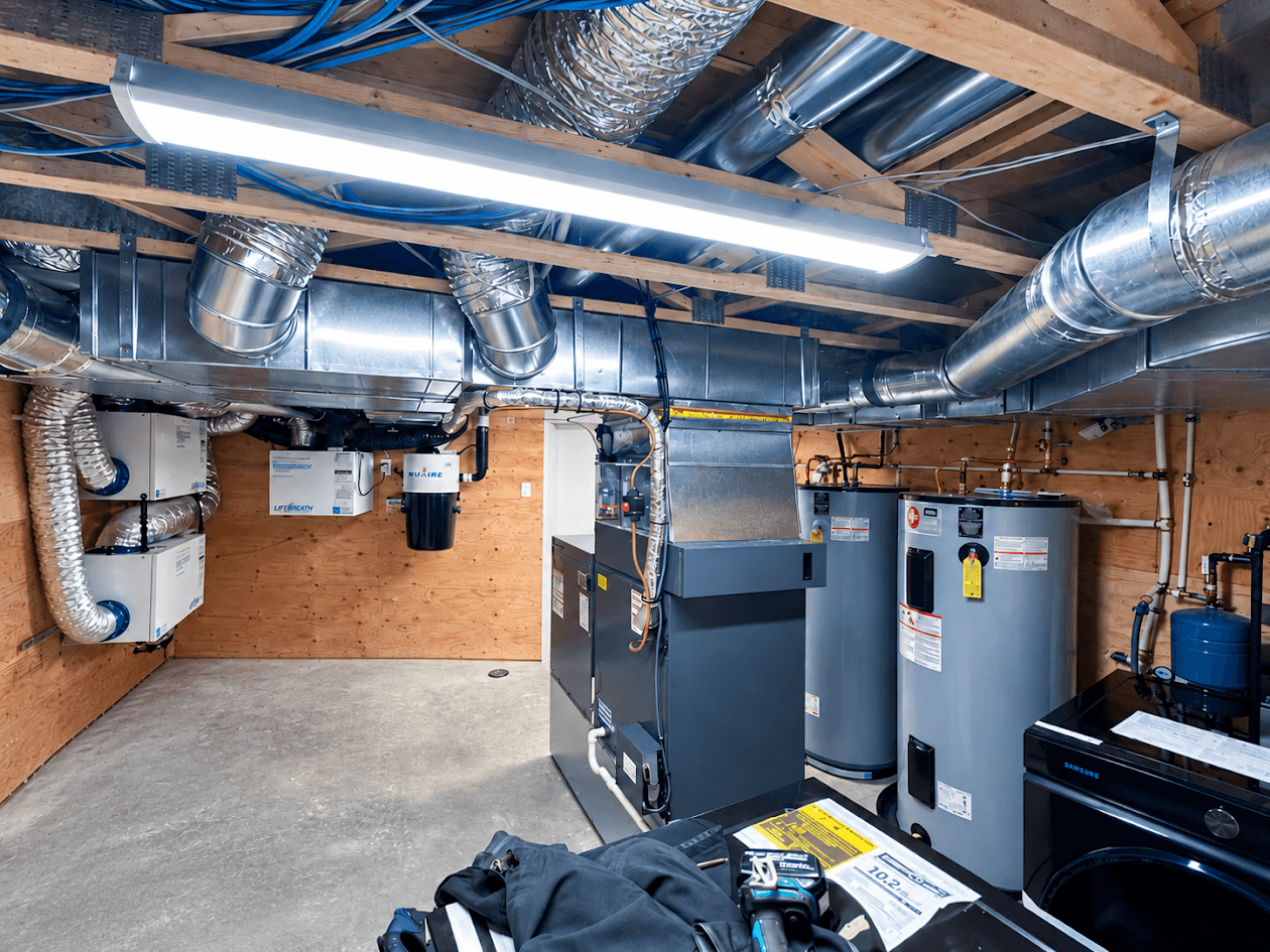 Residential mechanical room equipped with heating and ventilation system, metal ductwork, water heaters, air exchangers, exposed piping and technical equipment.