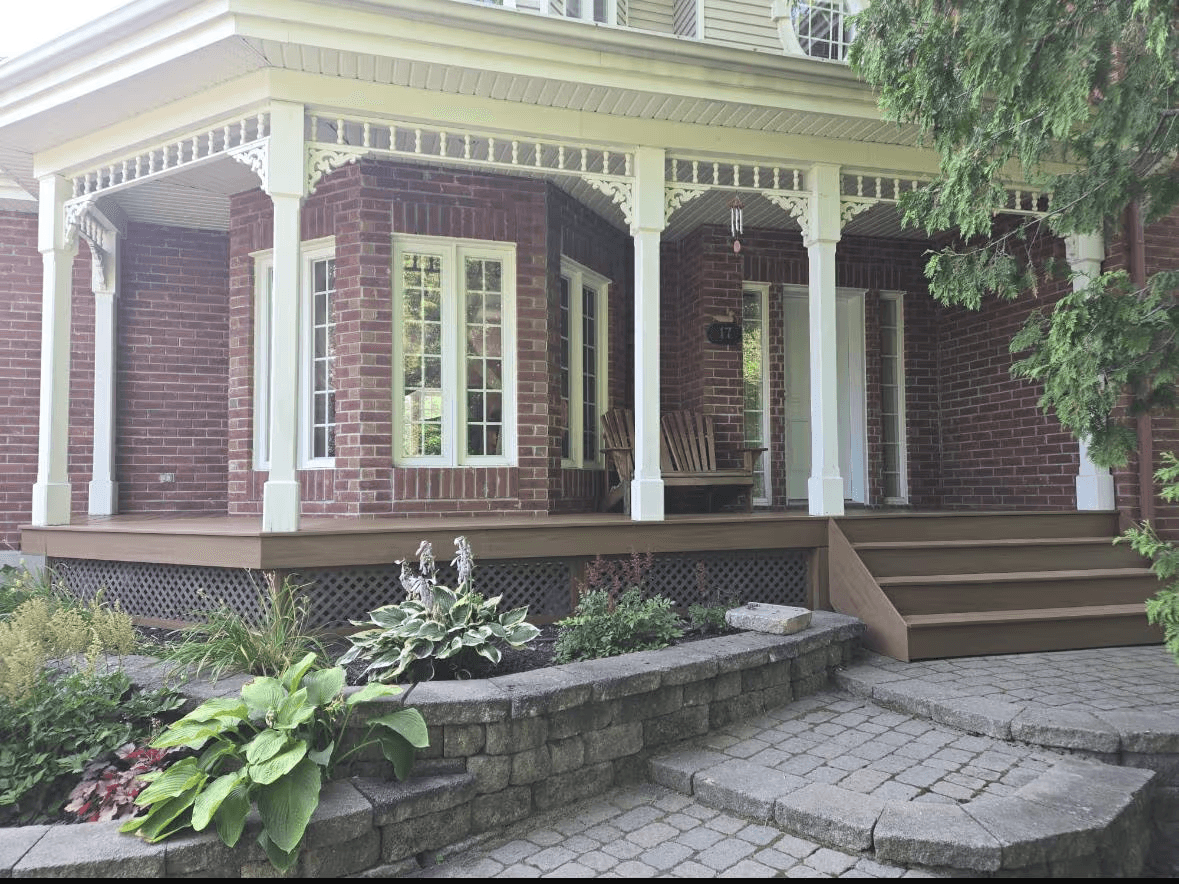 Brick house facade with a large covered porch, white columns, exterior stairs, interlocking pavers, retaining wall and landscaping