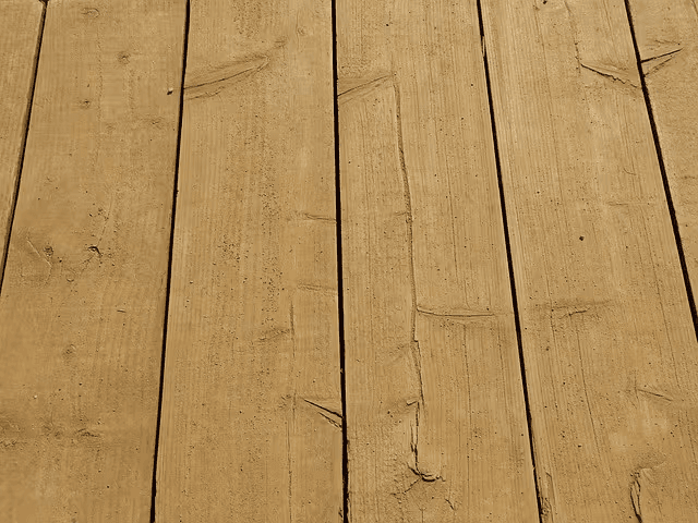 Close-up of natural beige wooden deck boards with visible grain and knots, arranged in parallel to create an outdoor decking surface.