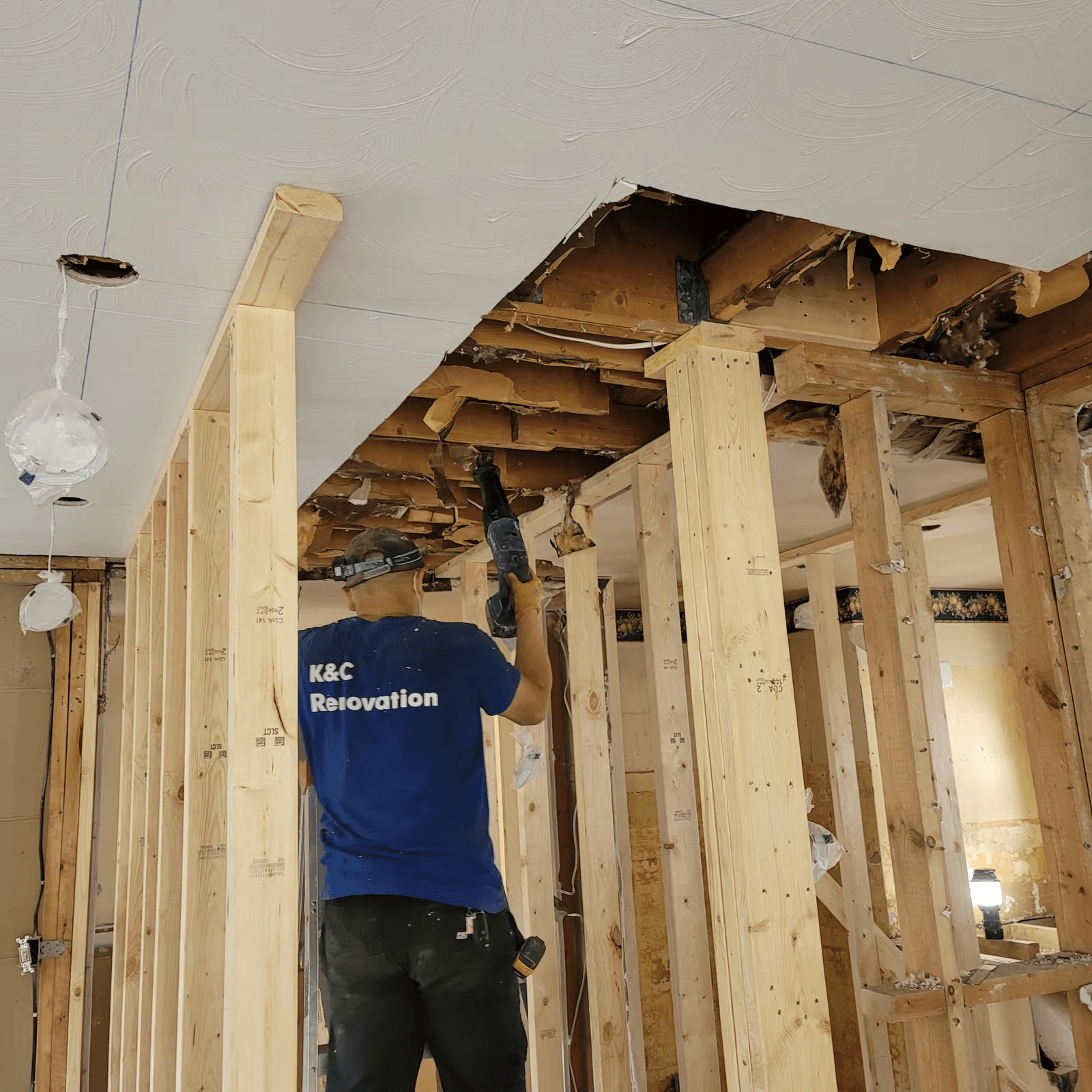 Interior renovation worker using a power tool beneath an opened ceiling, with new wood framing and exposed structural elements