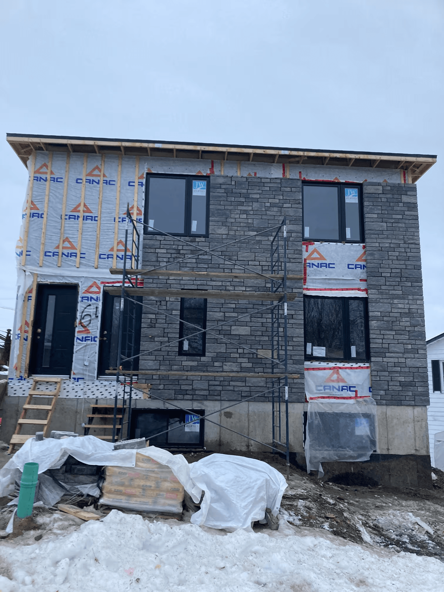 Construction of a new two-story house featuring grey exterior brick masonry installation, metal scaffolding, black windows and exposed wood framing