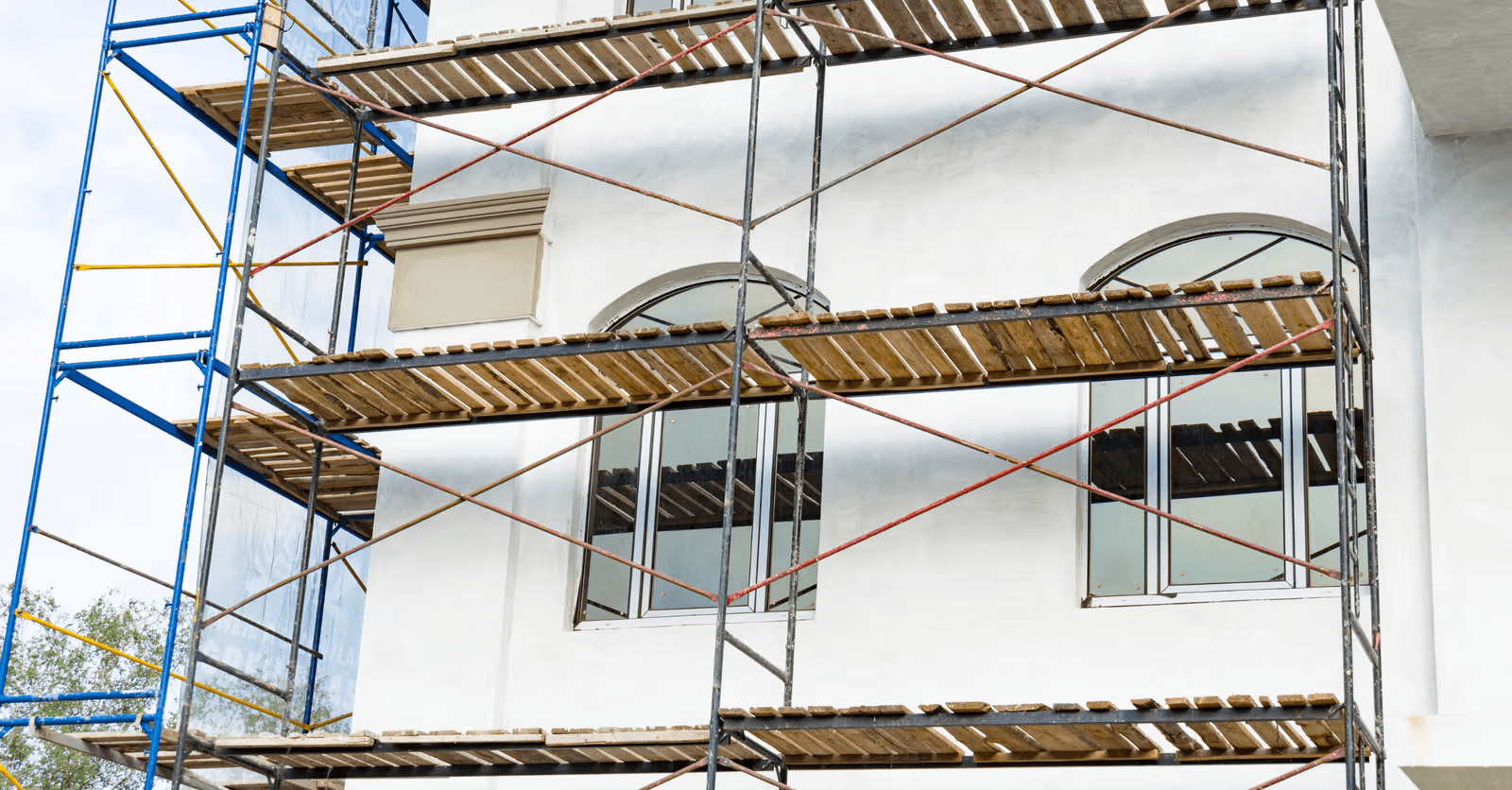 Renovation of a white exterior facade with scaffolding, large windows and exterior finishing work.