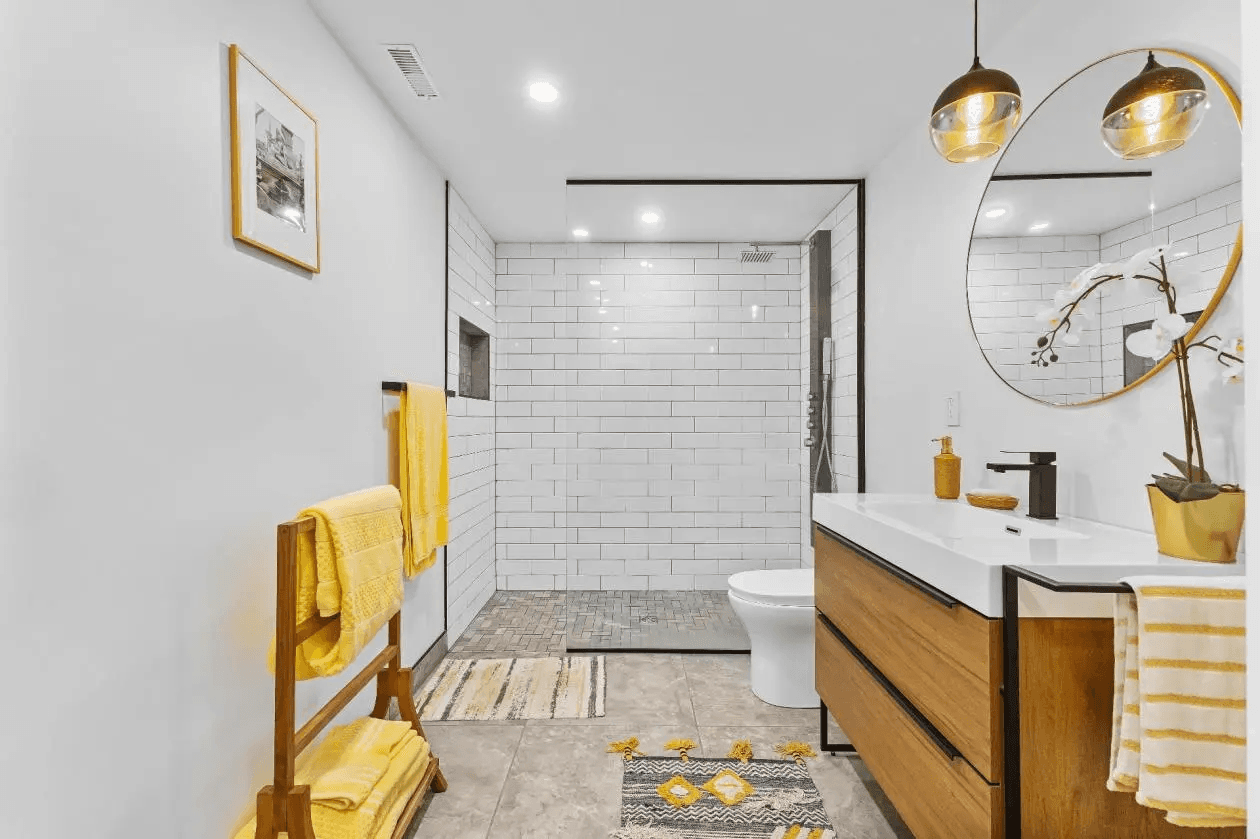 Bright bathroom with a walk-in shower surrounded by white subway tiles, a vessel sink on a wooden vanity, and a round mirror.