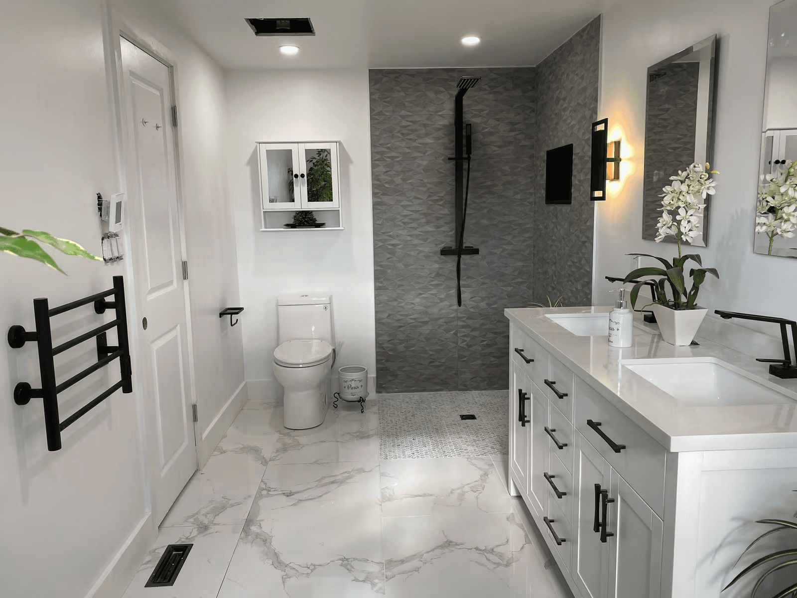 Modern renovated bathroom with a grey tiled walk-in shower, white double vanity, black fixtures and marble-look flooring