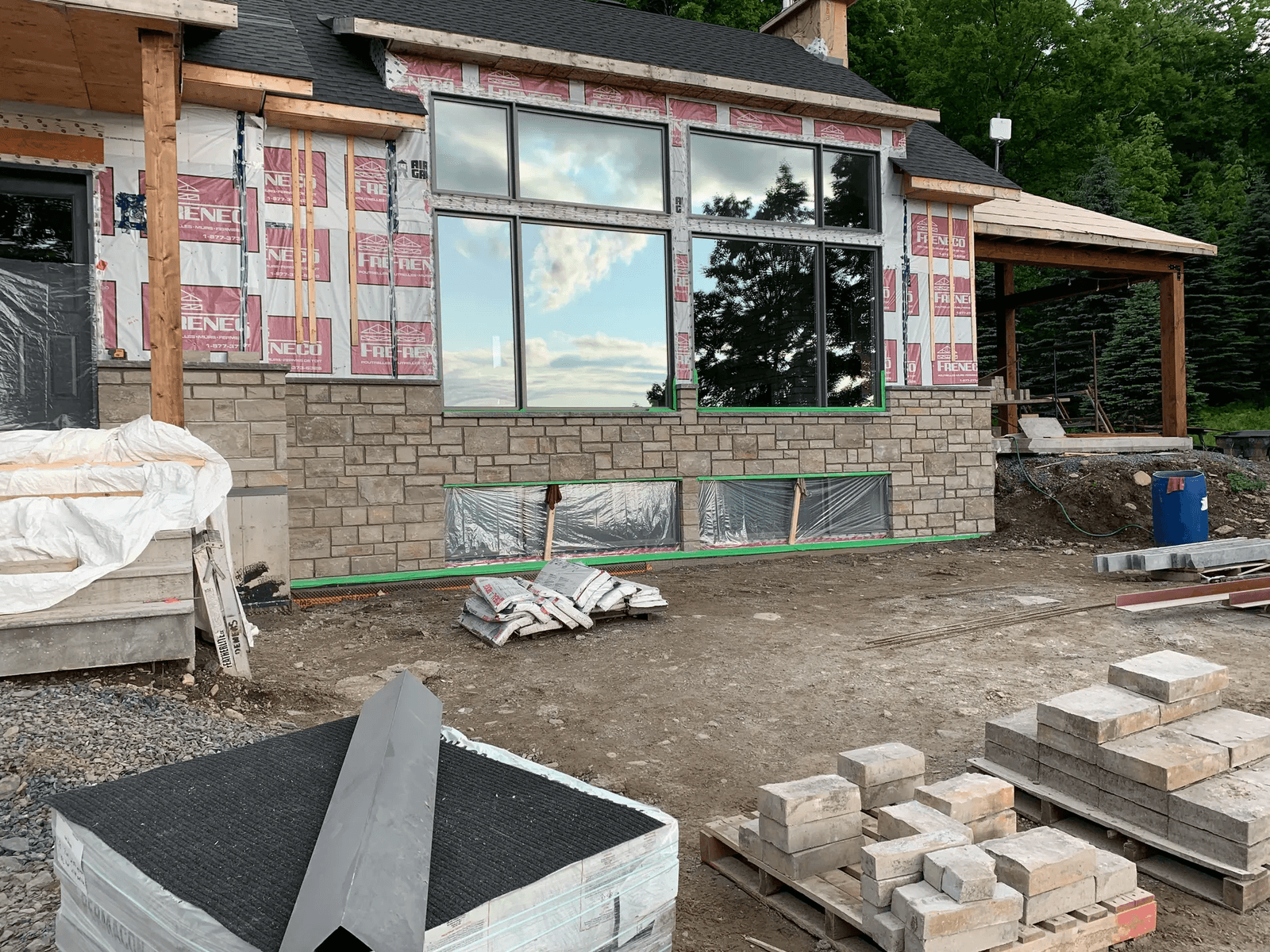 House under construction with partially installed stone siding, large windows, and construction materials on the ground