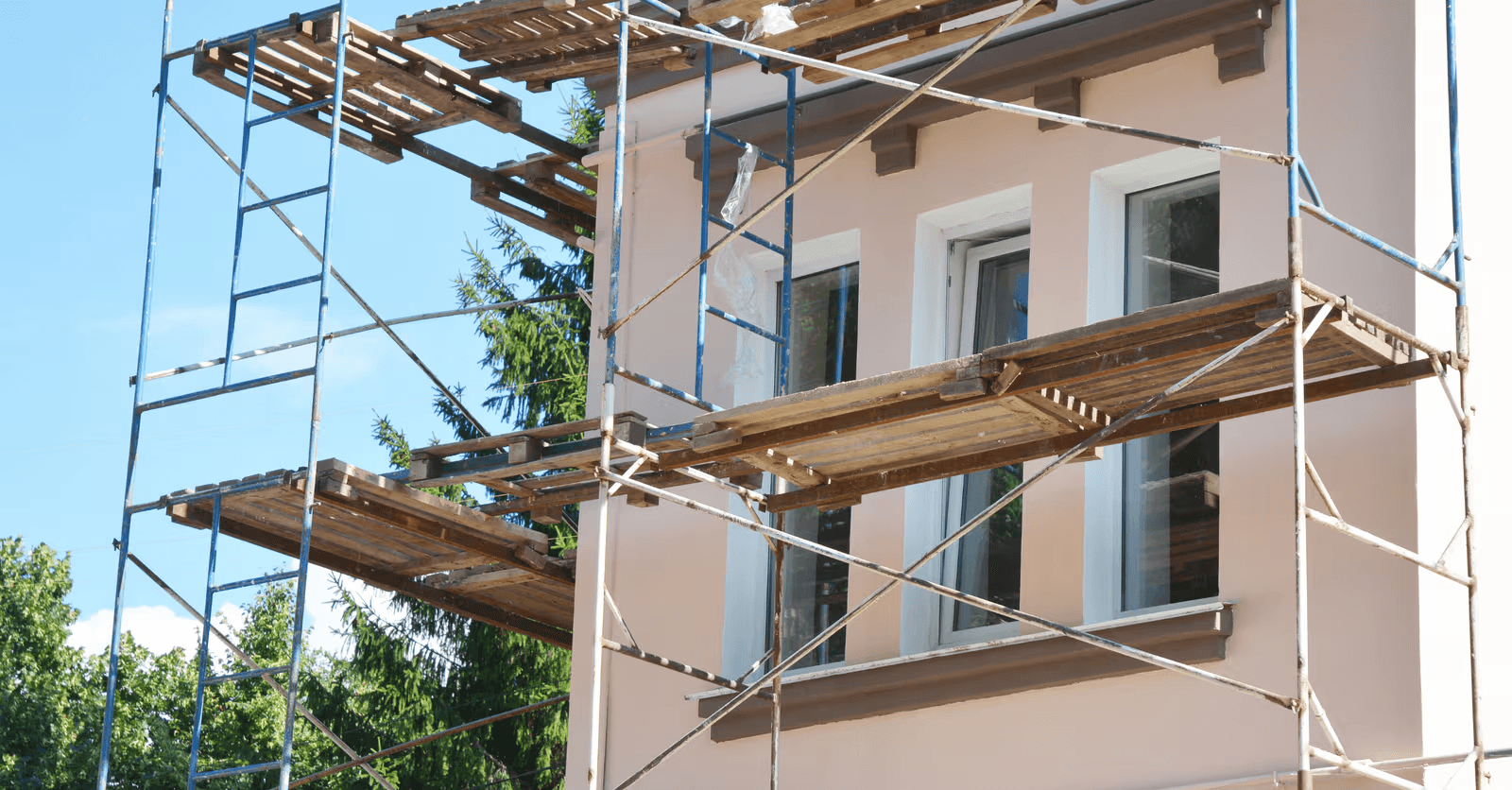 Residential facade undergoing exterior renovation with scaffolding, new finish coating and white-framed windows.