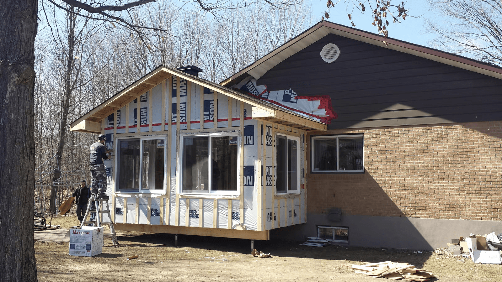 Residential home extension under construction with timber framing, exterior insulation, new windows and siding work on an existing house.