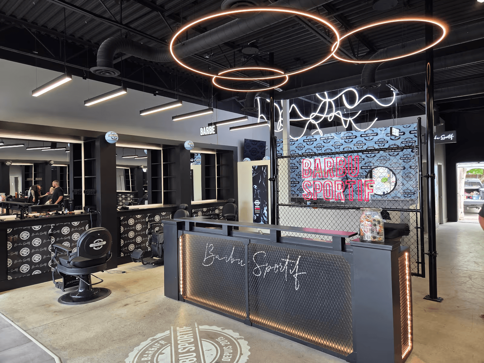 Modern barbershop interior with barber stations, chairs, reception counter, circular pendant lighting and industrial decor
