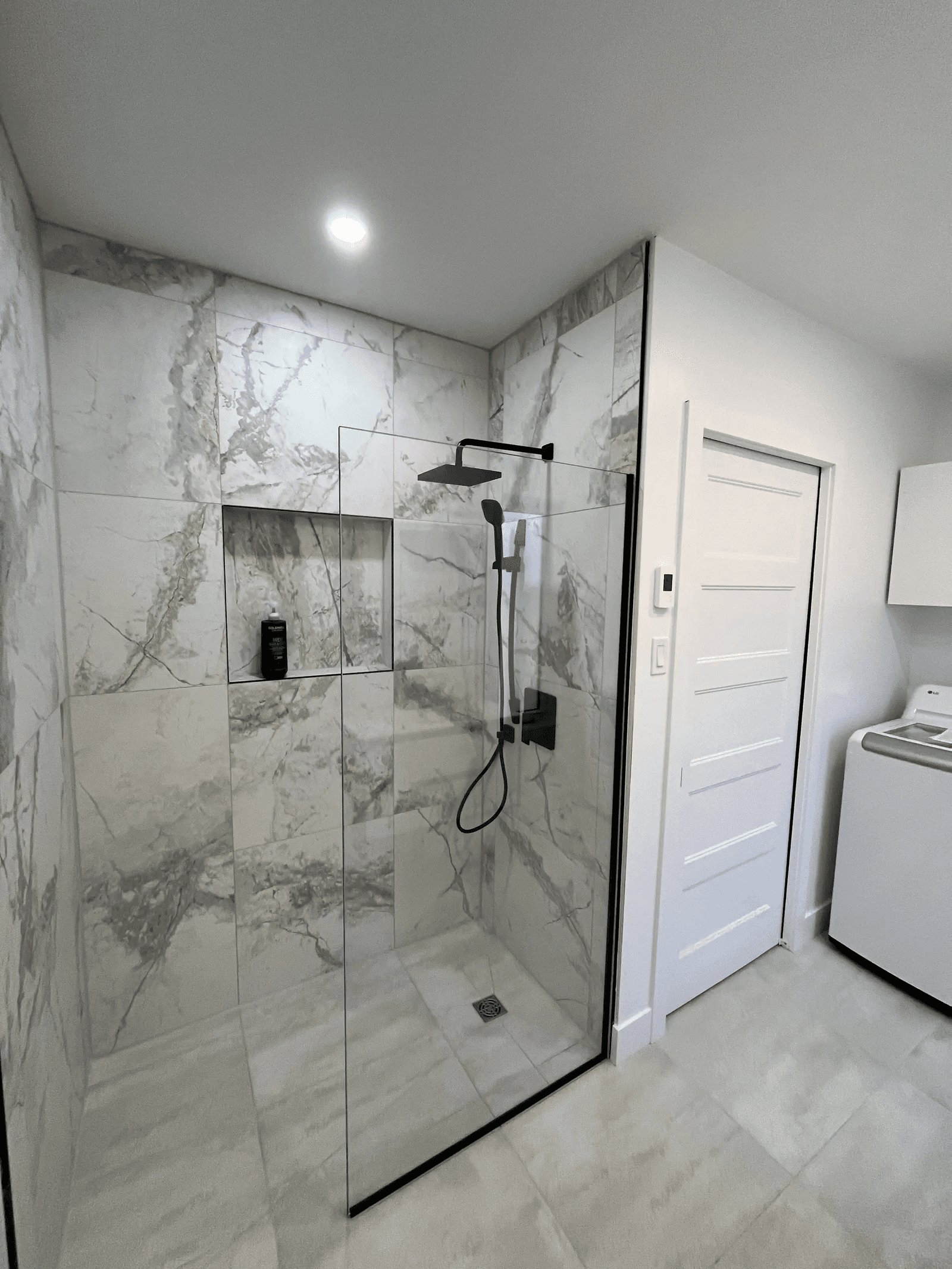 Modern walk-in shower with glass panels, white marble-look tiles, a recessed wall niche and black fixtures in a renovated bathroom