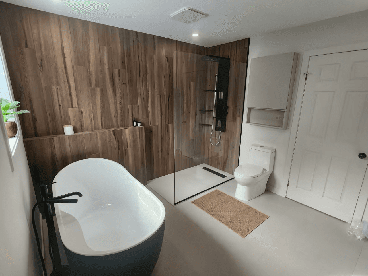 Modern bathroom with a freestanding bathtub, walk-in glass shower, wood-look wall covering, black fixtures and white toilet