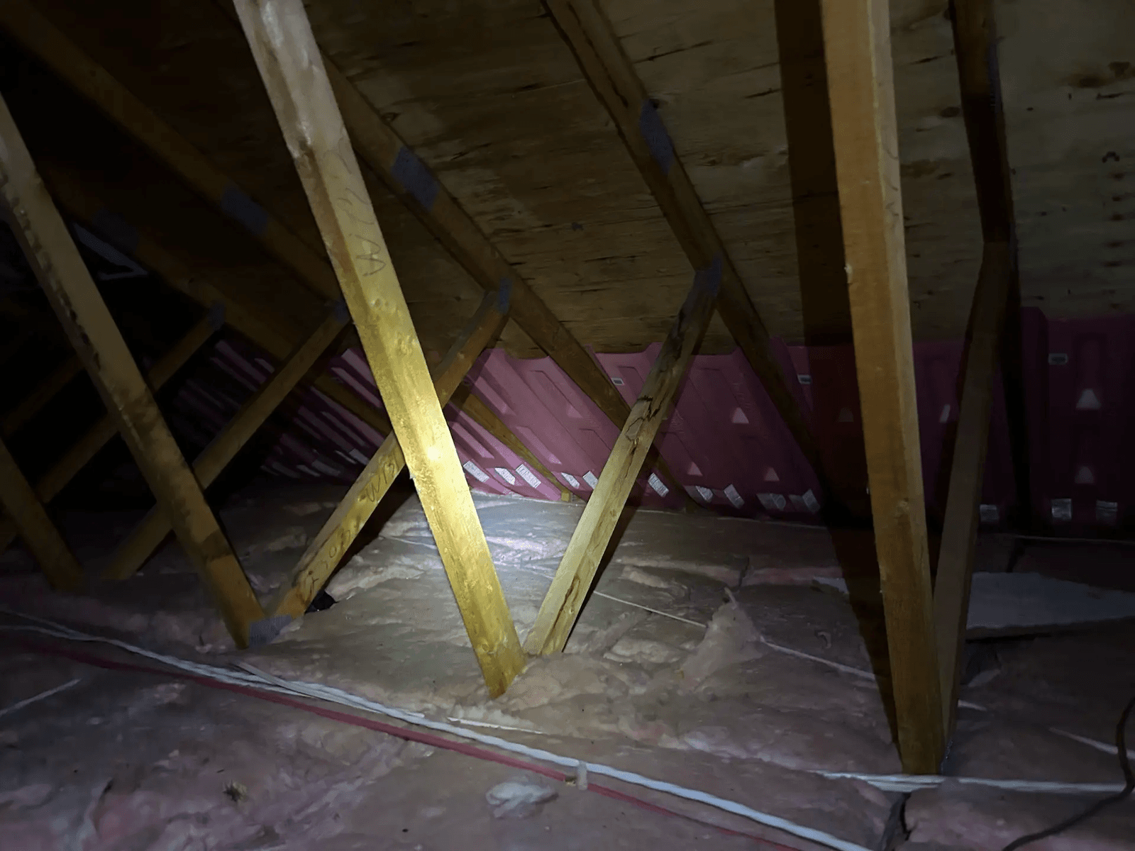 Residential attic with wood framing, fiber insulation between joists and flashlight inspection in a dark roof space