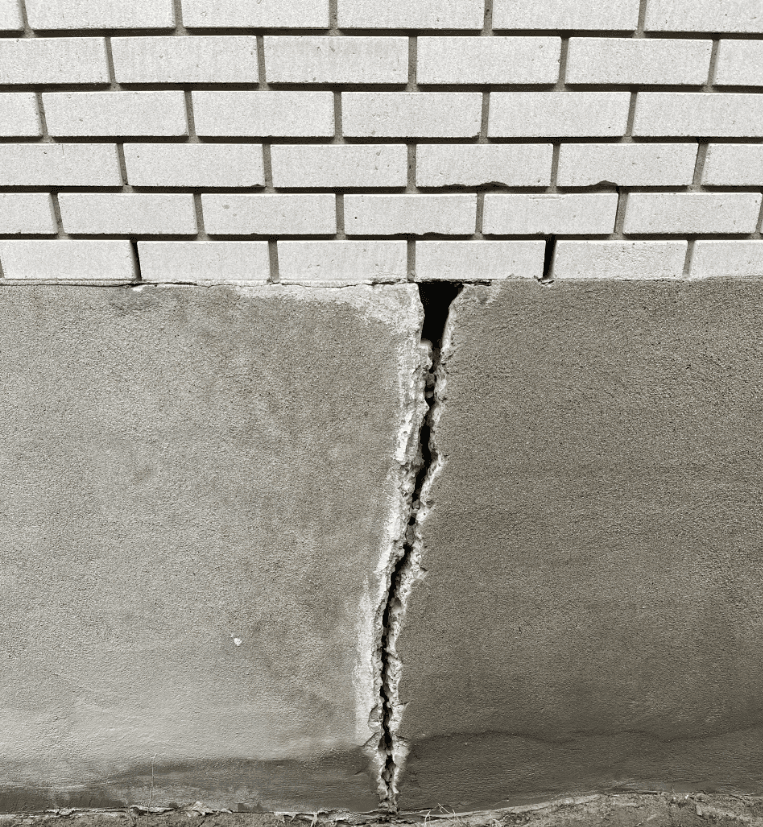 Vertical crack between the concrete foundation and brick wall of a residential home.