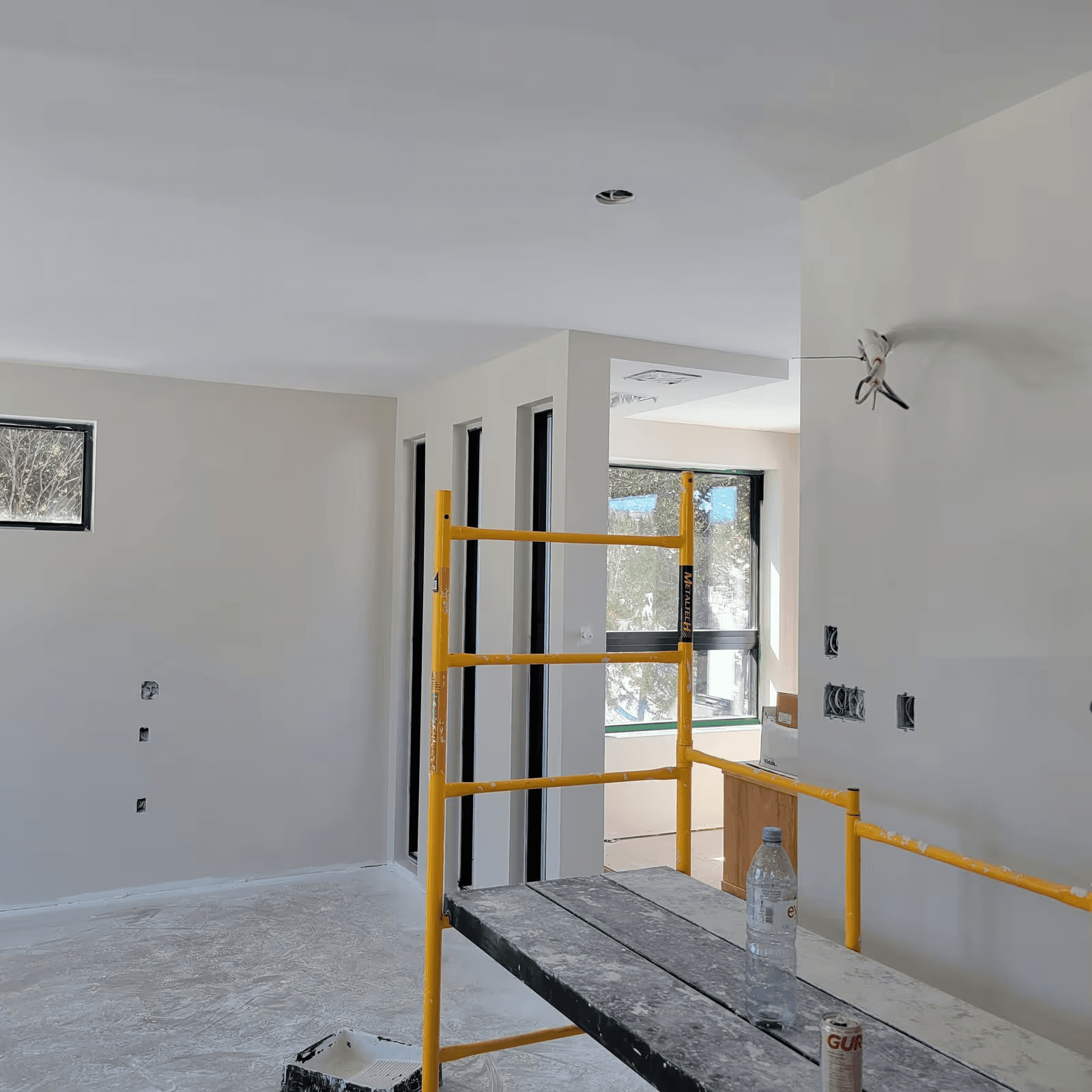 Residential room under renovation with freshly finished walls and ceiling, exposed electrical openings and indoor scaffolding for finishing work