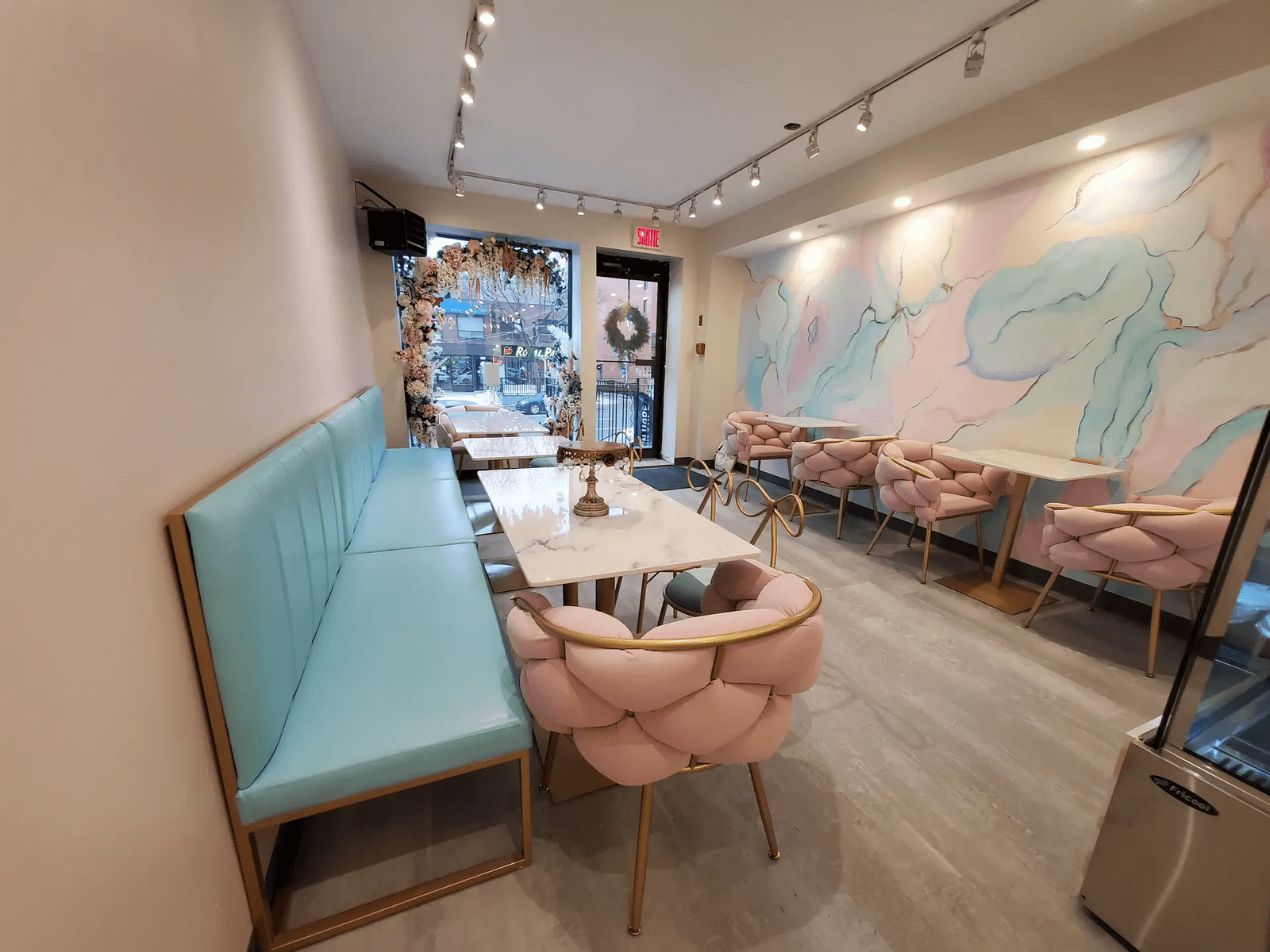Modern café or restaurant interior with turquoise bench seating, pink chairs, marble tables, track lighting and a pastel decorative wall mural