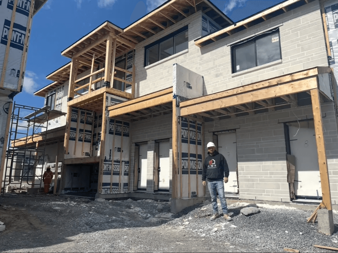 Construction of a multifamily residential building featuring grey exterior masonry blocks, exposed wood framing, balconies under construction and construction workers on site