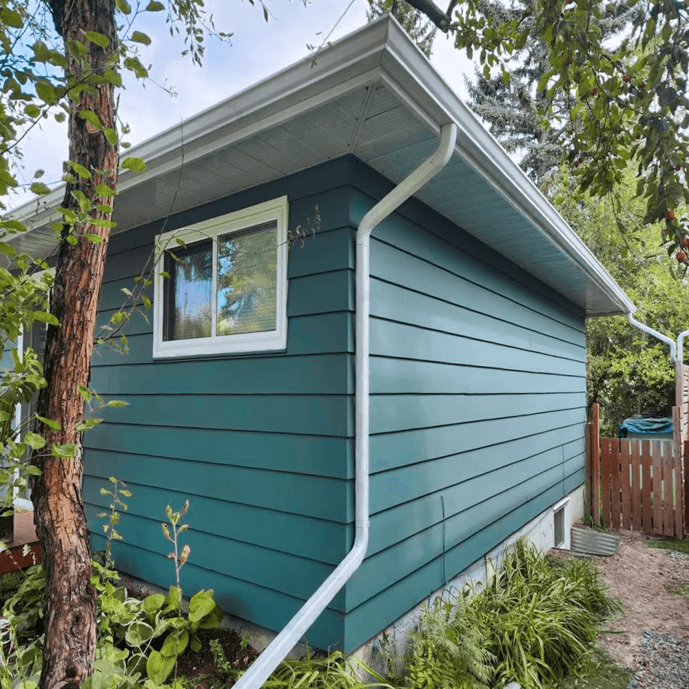 Teal blue exterior siding on a house with white window, gutters, downspout and soffits.