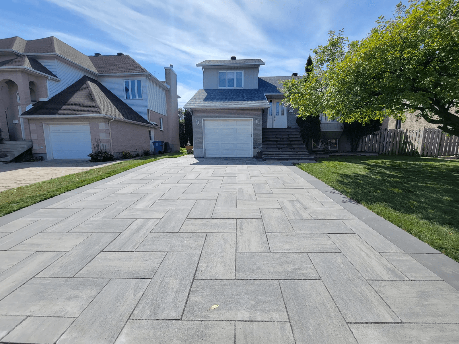 Modern residential driveway paved with grey interlocking pavers in front of a suburban house with built-in garage