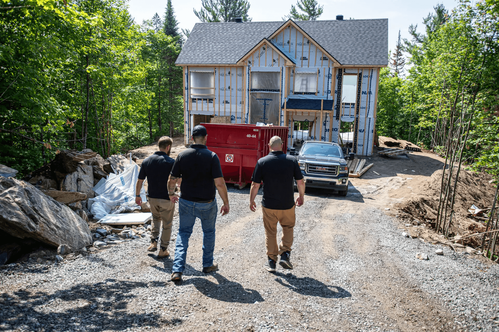 Three professionals inspecting a residential construction site with a house under construction surrounded by greenery.