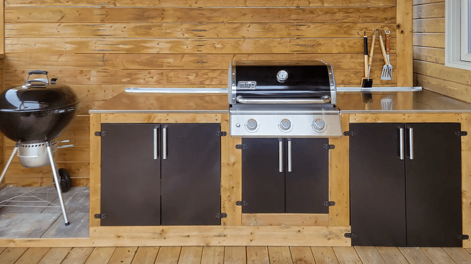 Outdoor wooden kitchen with built-in barbecue and stainless steel countertop.